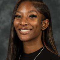 Person smiling in black shirt against gray background.